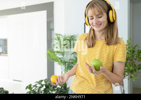 Happy woman wearing wireless headphones holding green apple and lemon Stock Photo