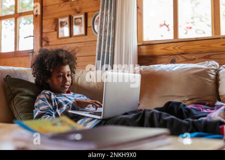 Boy using laptop resting on sofa at home Stock Photo