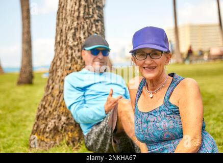 Middle Aged Senior Couple sitting on Grass in Park near the beach Stock Photo