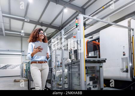 Smiling young engineer standing with tablet PC by machine in industry Stock Photo