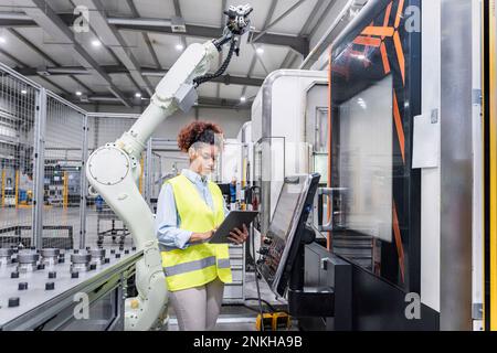 Young engineer using tablet PC by robotic arm at industry Stock Photo