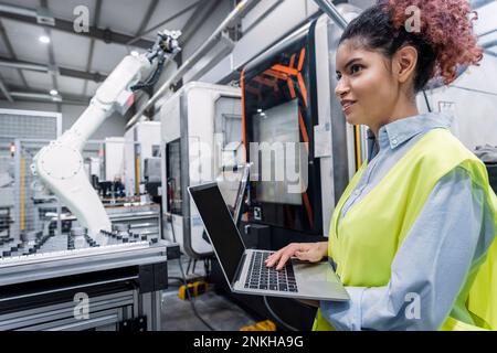 Happy young engineer standing with laptop in factory Stock Photo