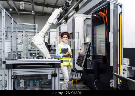Smiling engineer standing with tablet computer by machine in factory Stock Photo