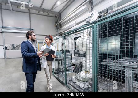Young engineers discussing over robotics arm in industry Stock Photo