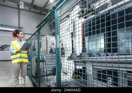 Young engineer using tablet PC by machine in factory Stock Photo