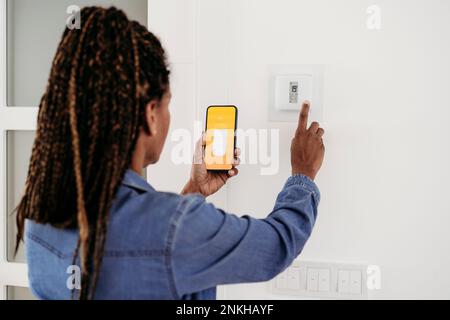 Mature woman adjusting thermostat through smart phone app Stock Photo
