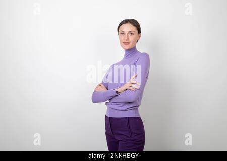 Smiling young woman standing with arms crossed over white background Stock Photo