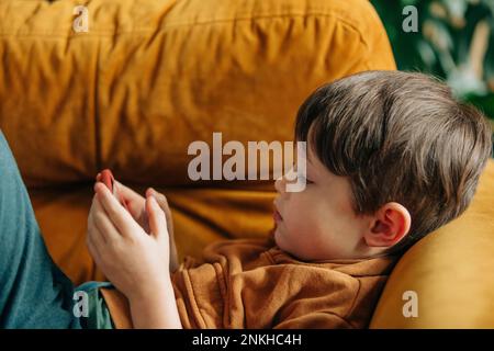 Boy using smart phone lying on sofa at home Stock Photo