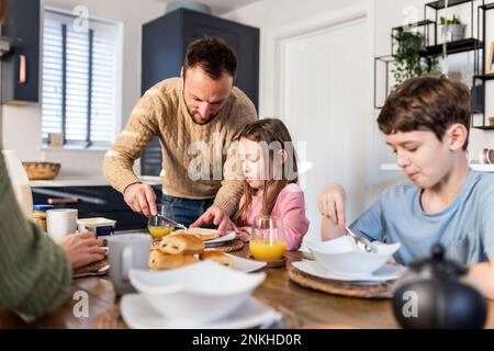 Father applying butter on bread by family having breakfast in kitchen Stock Photo