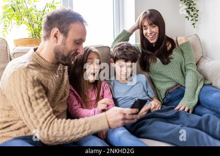 Happy family using smart phone on sofa at home Stock Photo