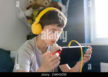 Boy wearing headphones playing video game on tablet PC at home Stock Photo