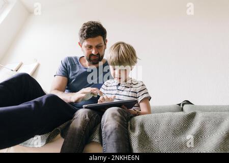 Father and son using tablet PC sitting at home Stock Photo
