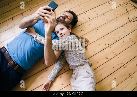 Daughter lying by father using smart phone at home Stock Photo