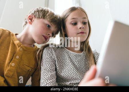 Brother and sister using tablet PC at home Stock Photo