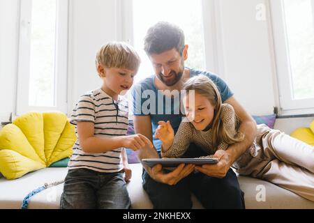 Son and daughter using tablet PC with father at home Stock Photo