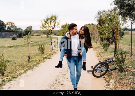 Boyfriend giving girlfriend piggyback ride on dirt road Stock Photo