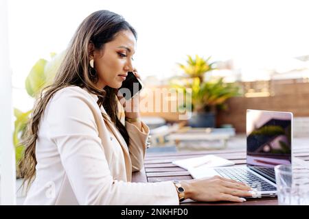 Freelancer talking on smart phone and using laptop Stock Photo