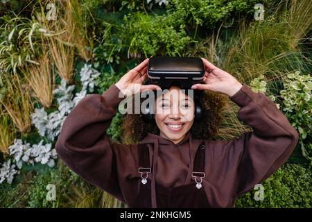 Smiling woman with VR goggles in front of plants Stock Photo