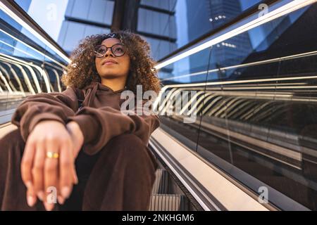 Thoughtful young woman sitting on escalator Stock Photo