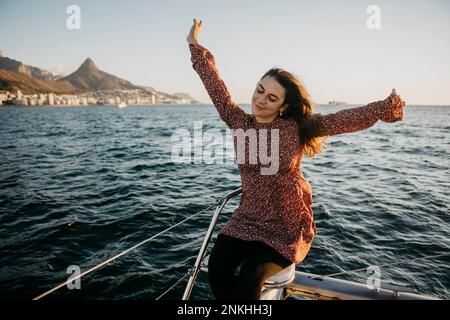 Young woman with arms raised sitting on boat in sea at weekend Stock Photo