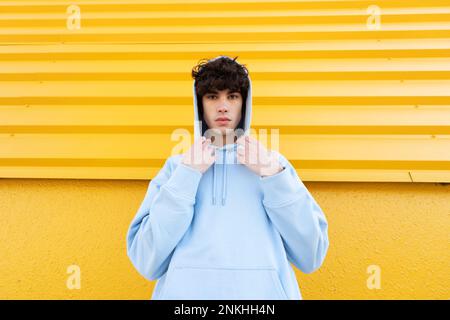 Young man wearing hooded shirt in front of yellow wall Stock Photo