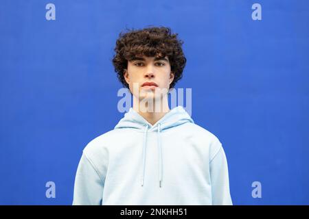 Confident man wearing hooded shirt in front of blue wall Stock Photo