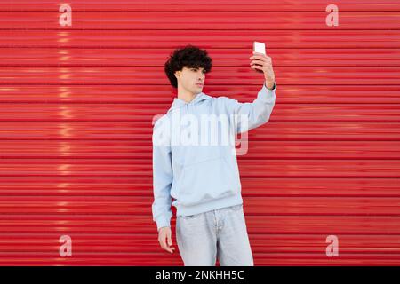 Young man taking selfie using smart phone in front of red wall Stock Photo