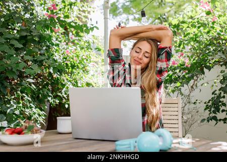 Freelancer stretching arms sitting with laptop at table Stock Photo