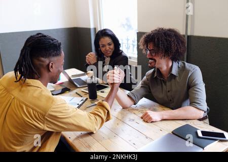 Businessmen arm wrestling with each other sitting at desk in office Stock Photo