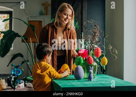 Smiling mother and son decorating table for Easter dinner at home Stock Photo