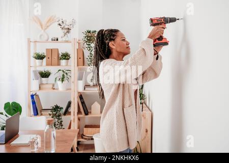 Woman using drill machine on wall at home Stock Photo