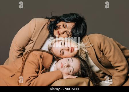 Teenage girl with woman and mother leaning head on each other against gray background Stock Photo