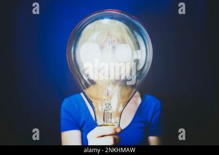 Woman holding large illuminated bulb against blue background Stock Photo