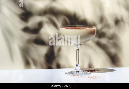 Brandy alexander alcoholic cocktail drink with cognac, cocoa liquor, cream, nutmeg and ice. Light beige background, hard light, shadow pattern Stock Photo