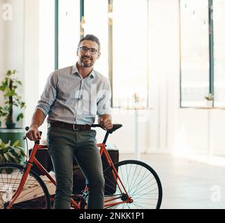 You wont find me late for work using a bicycle. Portrait of a mature businessman standing in a modern office with his bicycle. Stock Photo