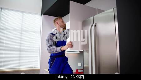 Male Carpenter Assembling White Cabinet On Wall In Kitchen Stock Photo