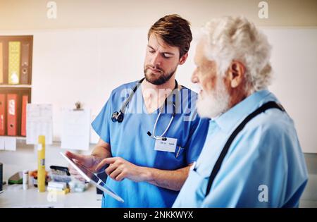 Hes using his tablet to explain the treatment methods available. a young doctor using a digital tablet to explain a diagnostic to a senior patient at Stock Photo