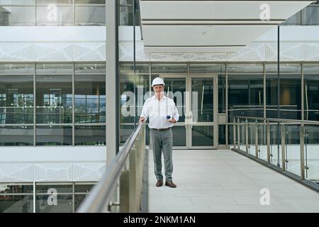 He knows what to do when it comes to building and development. Portrait of a cheerful professional male architect looking at the camera while holding Stock Photo
