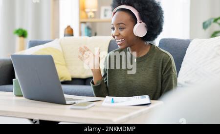 Woman talking on videocall using laptop and headphones while waving hello to friends online. Student making notes while communicating and learning new Stock Photo