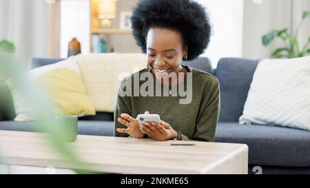 Excited black woman chatting in dating app using her phone at home. A young female online shopping happy about a purchase in her house. A lady Stock Photo