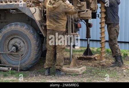 Team of workers with drilling rig on car are drilling artesian well for ...