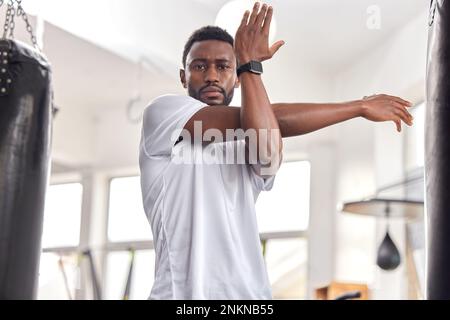 Stretching, fitness and portrait of a black man at the gym for training, muscle and arms warm up. Exercise, focus and African athlete preparing for a Stock Photo