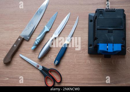 Sharpening a knife on an electric sharpener at home. Flatlay knife blade, scissors, sharpeners, dust flies on the machine. Stock Photo