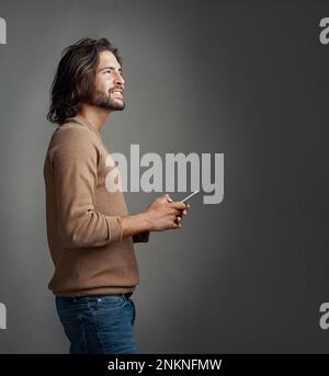 Should I have texted that. Studio shot of a handsome young man using a mobile phone against a gray background. Stock Photo