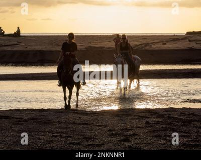 Horse riders cross a small river near the beach in Samara Costa Rica Stock Photo
