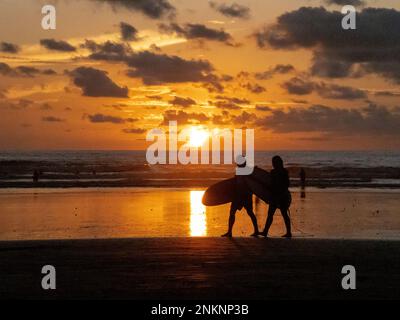 Two surfers in silhouette return from the water at sunset in Nosara in Costa Rica Stock Photo