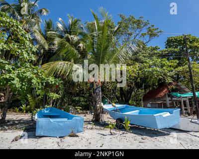 Two blue fishing boats sit on the beach under the palm trees on a beautiful day in Costa Rica near Nosara Stock Photo