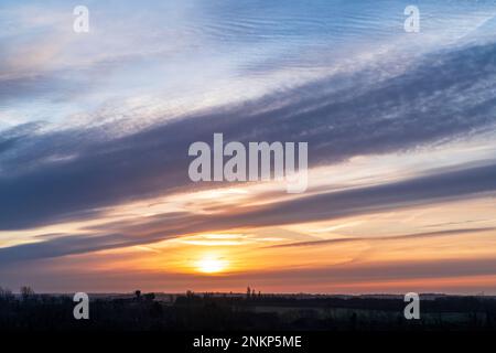 The sky over the south east Kent landscape on a winter's morning at Hillborough. Mainly low laying farmland with hedgerows and some scattered trees silhouetted against a cloudy sky with a hazy sun just above the horizon. Stock Photo