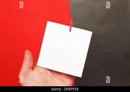 human hand holding sticker with empty mockup for your text hanging on the pin on red and black background Stock Photo
