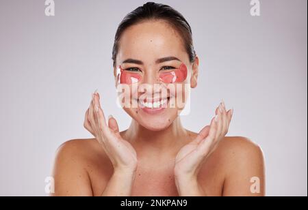 Asian woman, portrait smile and eye patches for skincare cosmetics, collagen or facial against a gray studio background. Happy female smiling in Stock Photo
